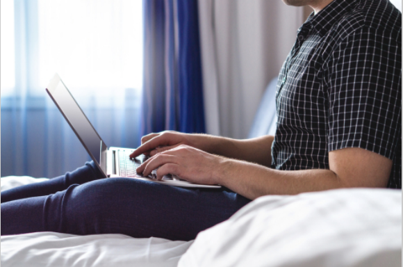 Man using laptop in hotel room or home bedroom